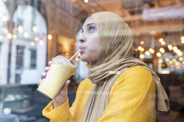 Junge Frau mit Hidschab trinkt Smoothie in einem Café - WPEF02713