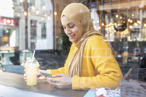 Porträt einer jungen Frau mit Smoothie und Smartphone in einem Café, lizenzfreies Stockfoto