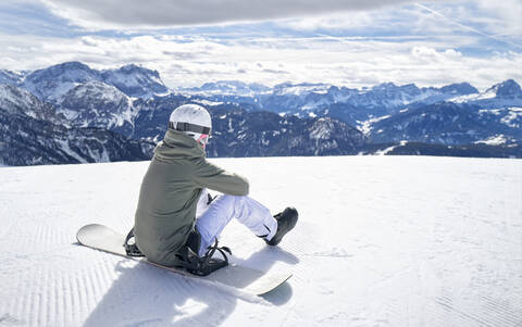 Smiling woman sitting with snowboard on viewpoint and enjoying view at distance stock photo