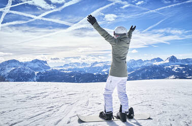 Ältere Frau mit Snowboard auf Skipiste mit erhobenen Armen - DIKF00381