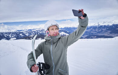 Lächelnde Snowboarderin macht ein Selfie mit ihrem Smartphone - DIKF00385