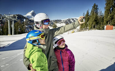 Mutter mit ihren Kindern, die ein Selfie auf der Skipiste machen - DIKF00388