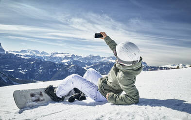 Snowboardfahrende Frau macht ein Selfie im Schnee - DIKF00392