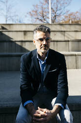 Gray-haired businessman sitting on stairs outdoors - JRFF04183