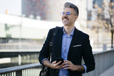 Smiling gray-haired businessman with cell phone in the city - JRFF04195