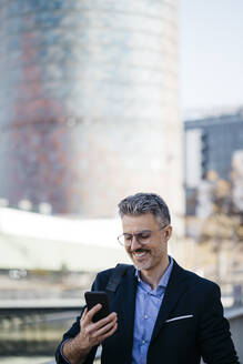 Smiling gray-haired businessman in the city using cell phone - JRFF04196