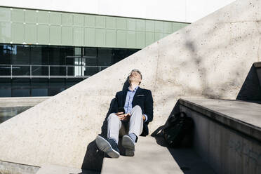 Gray-haired businessman relaxing on stairs in the city - JRFF04199
