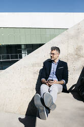 Gray-haired businessman sitting on stairs in the city - JRFF04201