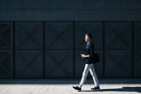 Gray-haired businessman walking along a building in the city stock photo