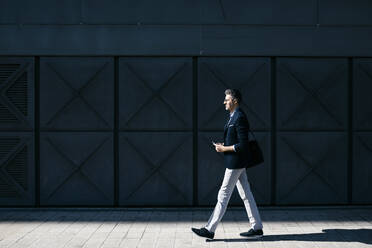 Gray-haired businessman walking along a building in the city - JRFF04210