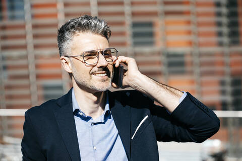 Porträt eines lächelnden grauhaarigen Geschäftsmannes am Telefon in der Stadt, lizenzfreies Stockfoto