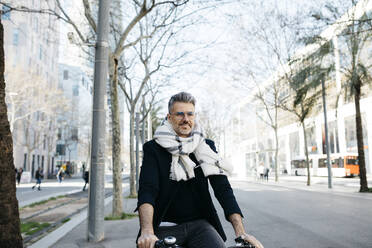 Gray-haired businessman riding bicycle in the city - JRFF04225