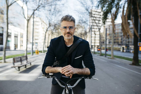 Portrait of a gray-haired businessman with bicycle in the city - JRFF04235