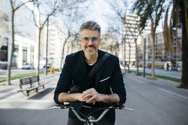 Portrait of a gray-haired businessman with bicycle in the city - JRFF04236