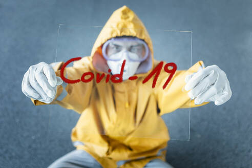 Portrait of man wearing protective clothing holding 'Covid 19' sign - WVF01448