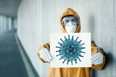 Porträt eines Mannes in Schutzkleidung, der ein Schild mit der Darstellung eines Virus hält - WVF01449