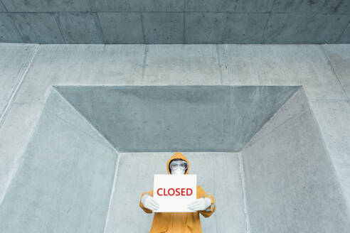 Portrait of man wearing protective clothing holding a 'closed' sign - WVF01467