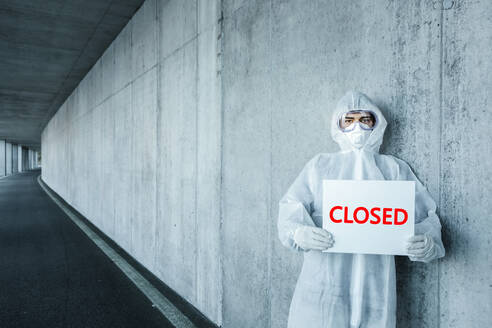 Portrait of man wearing protective clothing holding a 'closed' sign - WVF01499