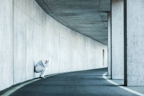 Despaired man wearing protective clothing leaning against concrete wall in a tunnel stock photo