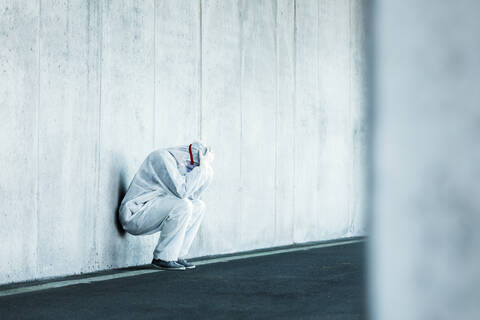 Despaired man wearing protective clothing leaning against concrete wall stock photo