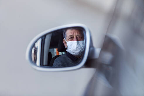 Reflection of senior man wearing mask in wing mirror of a car - WVF01521