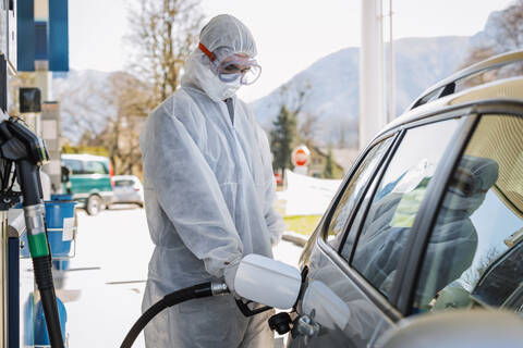 Mann in Schutzkleidung beim Betanken eines Autos an einer Tankstelle, lizenzfreies Stockfoto