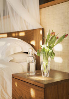 Tulpenstrauß und Wasserkrug auf dem Nachttisch in einem ruhigen Schlafzimmer - HOXF05225