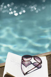 Heart-shape sunglasses on book at sunny, idyllic summer poolside - HOXF05298