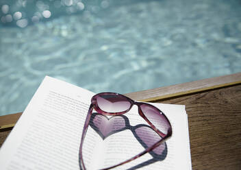 Heart-shape sunglasses on book at sunny poolside - HOXF05300