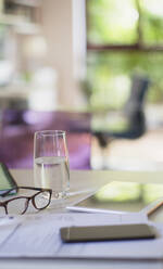 Water glass and eyeglasses on table with paperwork - HOXF05330