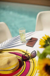 Sonnenhut und Sonnenbrille auf dem Terrassentisch im Sommer am Pool - HOXF05334