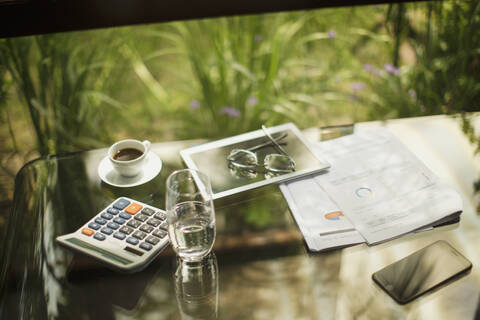 Taschenrechner und digitales Tablet auf dem Tisch mit Kaffee und Papierkram, lizenzfreies Stockfoto