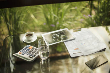 Taschenrechner und digitales Tablet auf dem Tisch mit Kaffee und Papierkram - HOXF05341