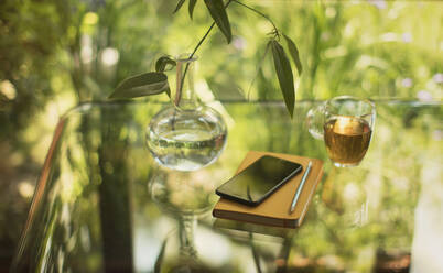 Tee und Smartphone auf dem Tisch mit Notizbuch und Vase - HOXF05349