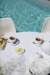 Teeservice auf dem sonnigen Terrassentisch im Sommer am Pool - HOXF05359
