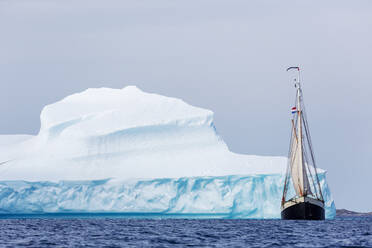 Schiff fährt entlang eines majestätischen Eisbergs auf dem Atlantischen Ozean in Grönland - HOXF05369