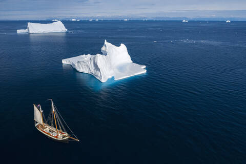 Schiff fährt an Eisbergen vorbei auf dem sonnigen blauen Ozean Grönlands, lizenzfreies Stockfoto