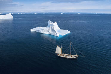 Schiff fährt an Eisberg vorbei auf sonnigem blauen Atlantik Grönland - HOXF05377