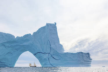 Schiff fährt hinter einem majestätischen Eisbergbogen auf dem Atlantik Grönland - HOXF05394