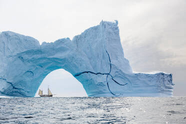 Schiff fährt hinter einem majestätischen Eisbergbogen auf dem Atlantik Grönland - HOXF05408