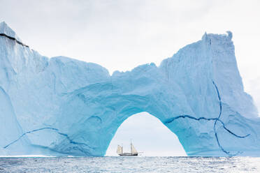 Schiff fährt hinter einem majestätischen Eisbergbogen auf dem Atlantik Grönland - HOXF05410