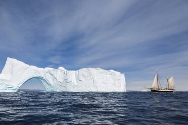 Schiff fährt auf sonnigen majestätischen Eisberg mit Bogen Grönland - HOXF05411