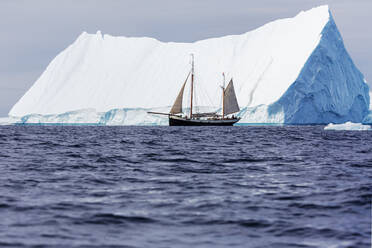 Schiff fährt an einem majestätischen Eisberg auf dem sonnigen Atlantik vorbei Grönland - HOXF05430