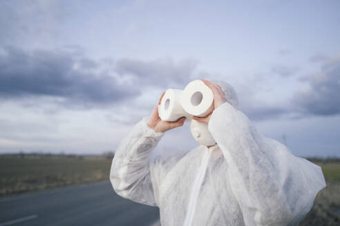 Mann mit Schutzanzug und Maske benutzt Toilettenpapier wie ein Fernglas - EYAF00960