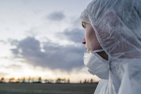 Portrait of man wearing protective suit and mask looking at sunset - EYAF00976