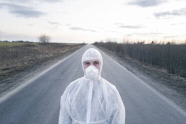 Porträt eines Mannes mit Schutzanzug und Maske, der auf einer Landstraße steht - EYAF00978