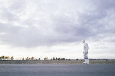 Man wearing protective suit and mask at the roadside of a country road - EYAF00979