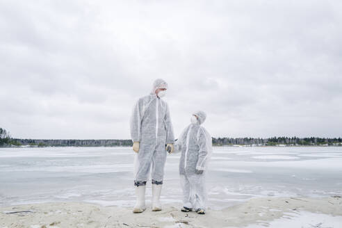 Vater und Sohn in Schutzanzügen stehen am zugefrorenen Fluss - EYAF00983