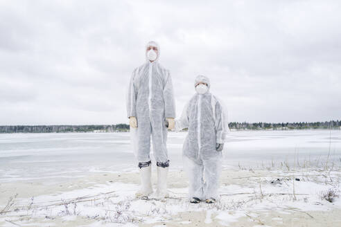 Vater und Sohn in Schutzanzügen stehen am zugefrorenen Fluss - EYAF00987