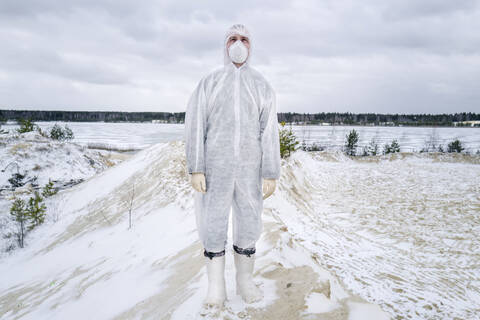 Mann mit Schutzanzug und Maske steht in einer ländlichen Winterlandschaft, lizenzfreies Stockfoto